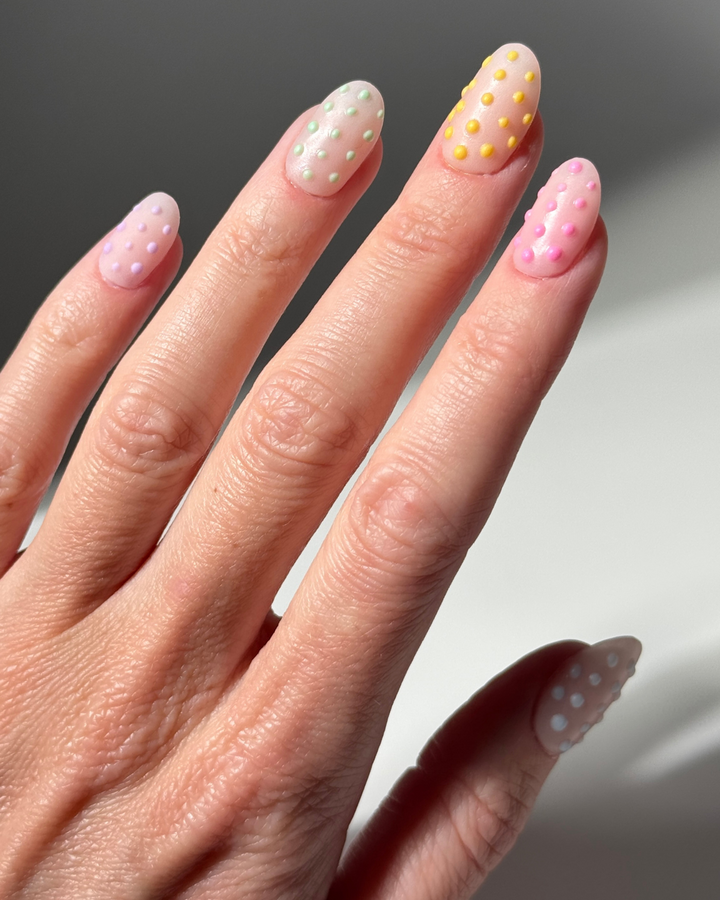 Hand mit aufwendigem 3D Polka-Dots Nageldesign. Frühlingshafte und pastellige Farben wie lila, grün, gelb, pink und blau. 
