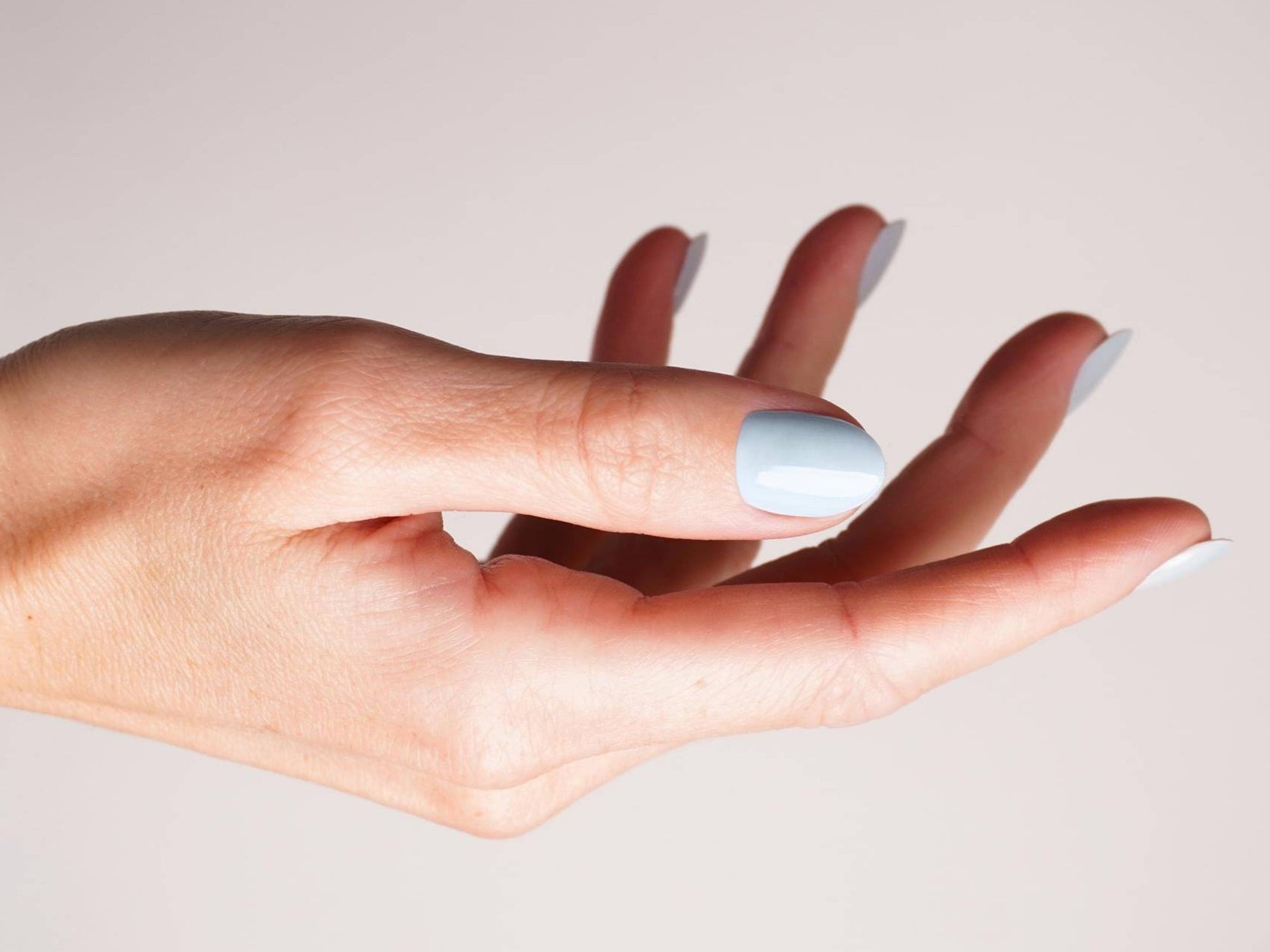 Hand mit hellblauen Gel Strips vor weißem Hintergrund, Fokus auf den Daumen.