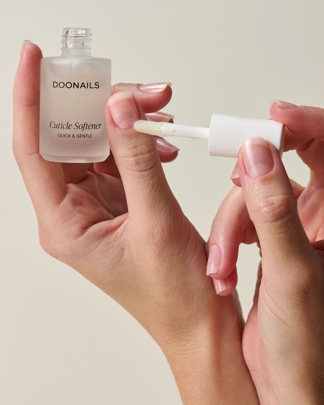 Zwei Hände, von denen eine Hand den Nagelhautentferner in der Hand hält und die andere es auf den Daumen aufträgt.