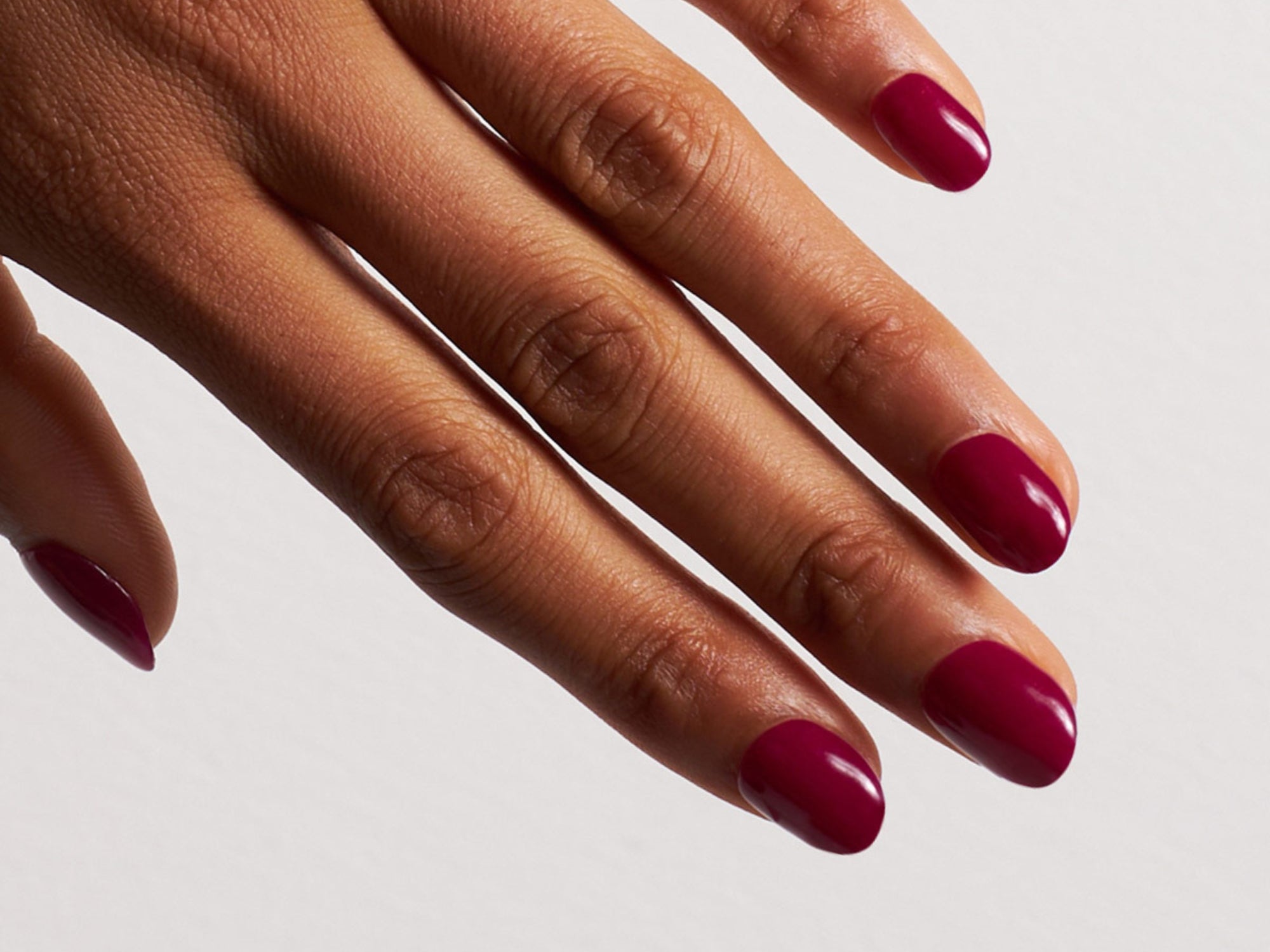 Hand mit dunkelroten Dipping Powder Nägel vor weißem Hintergrund.