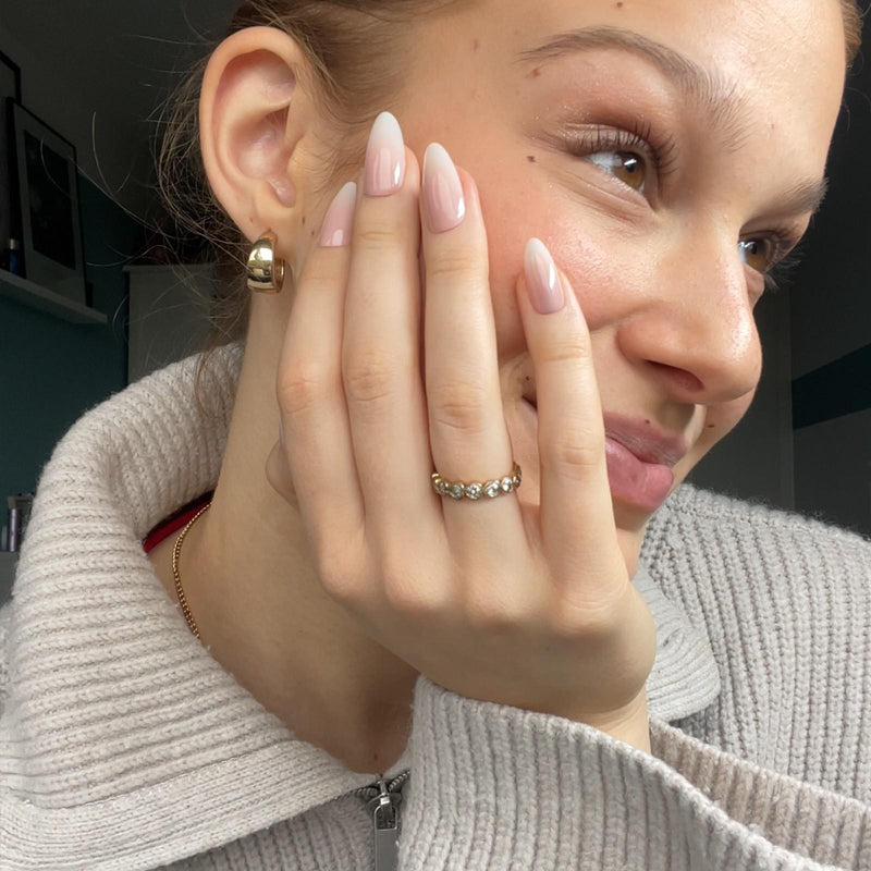 Lächelnde Frau stützt ihren Kopf auf der Hand mit Babyboomer Soft Gel Press ons auf und trägt einen goldenen Ring.