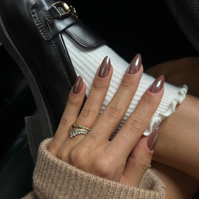 Eine Hand mit braunen Soft Gel Press Ons liegt auf dem Fußknöchlen. Getragen wird eine weiße Socke und schwarze Loafer.