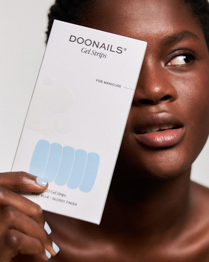 Frau mit dunklen Haaren hält eine hellblaue Gel Strips Verpackung vor ihr Gesicht. 