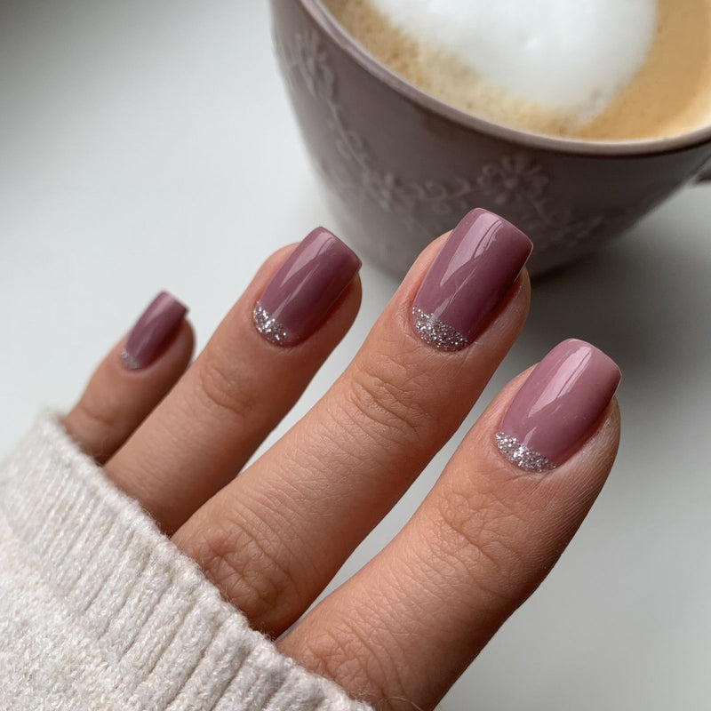 Lila Dipping Powder Nägel mit silbernem Glitzer am Nagelhautrand, im Hintergrund eine Kaffeetasse auf dem Tisch.