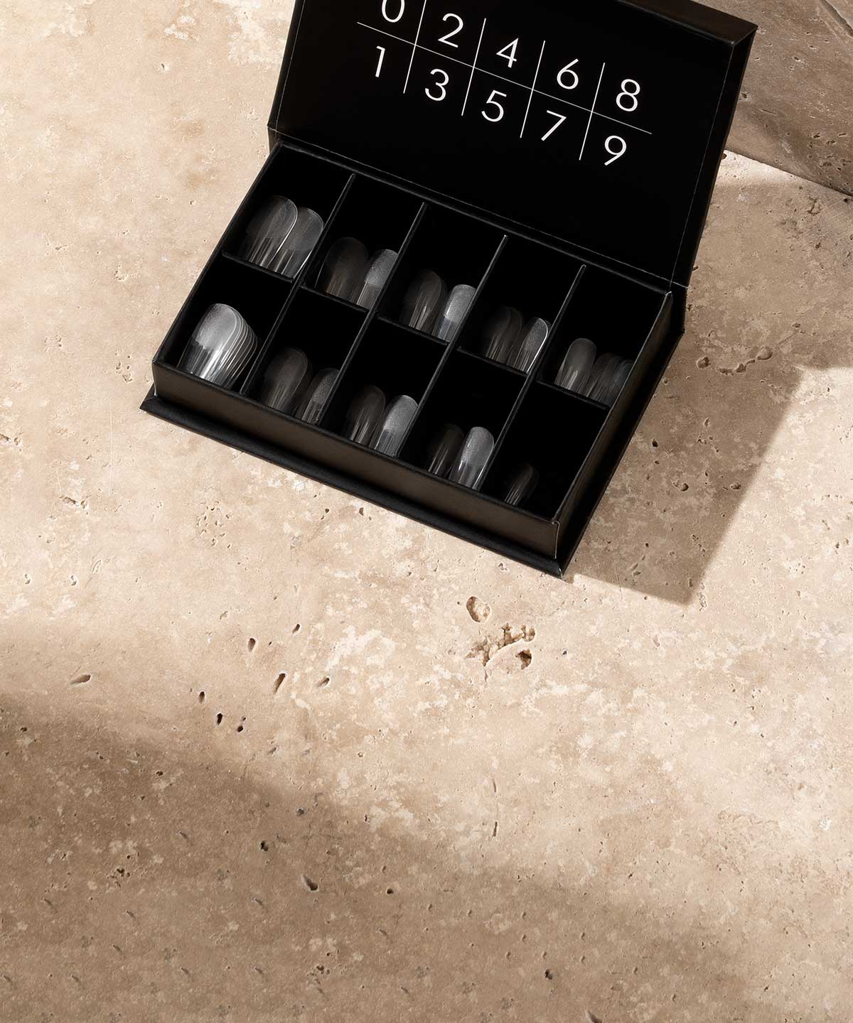 Aufgeklappte Box mit Nagelverlängerungs-Tips auf beigem Betonstein.