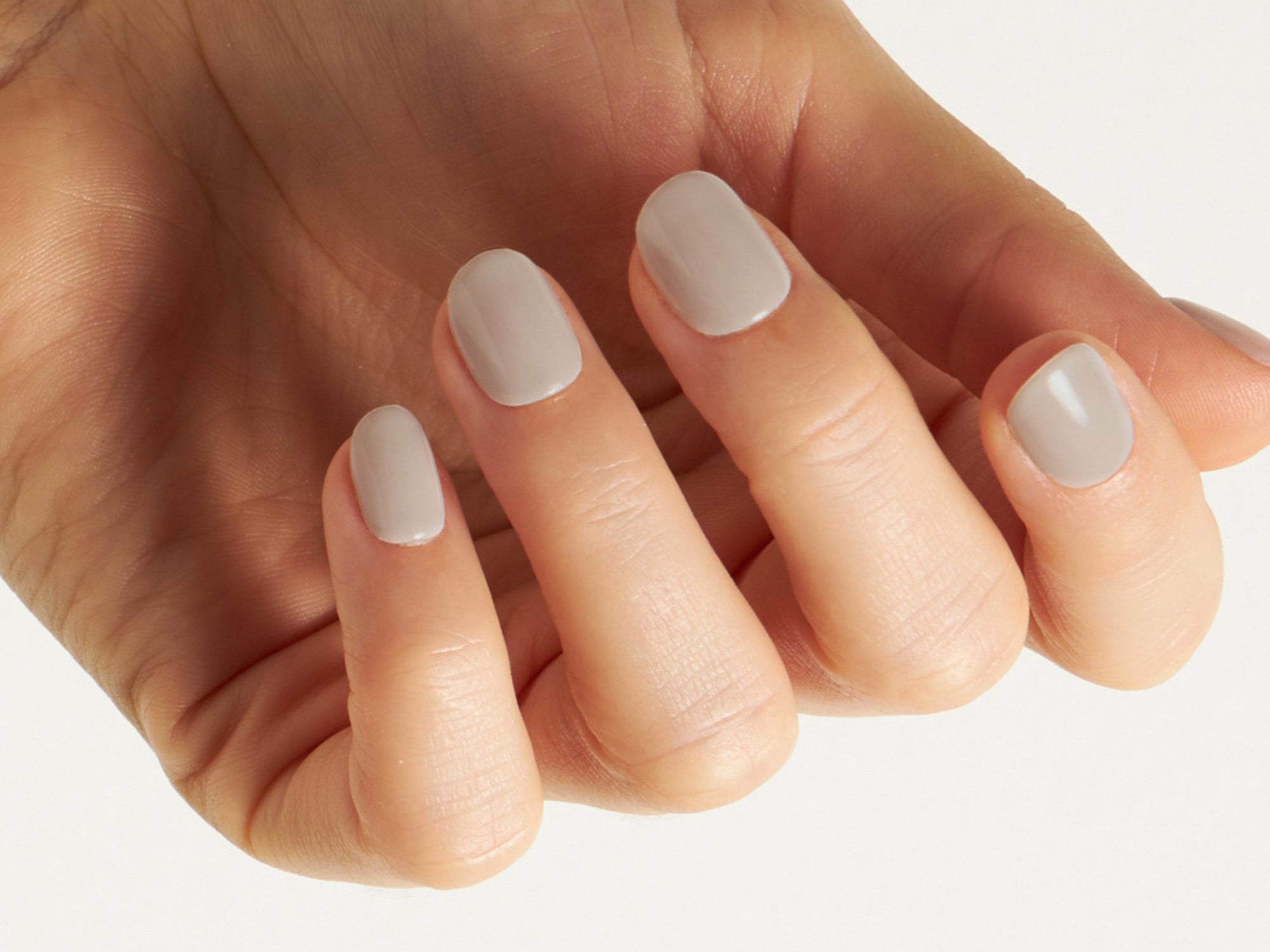 Hand mit nude farbenen Dipping Powder Nägeln vor weißem Hintergrund.