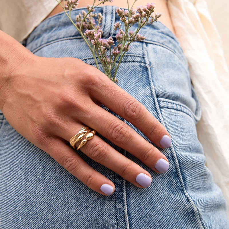 Hand mit pastell-lila Gel Strips und goldenem Ring steckt kleine Blumen in die hintere Hosentasche einer Jeans.