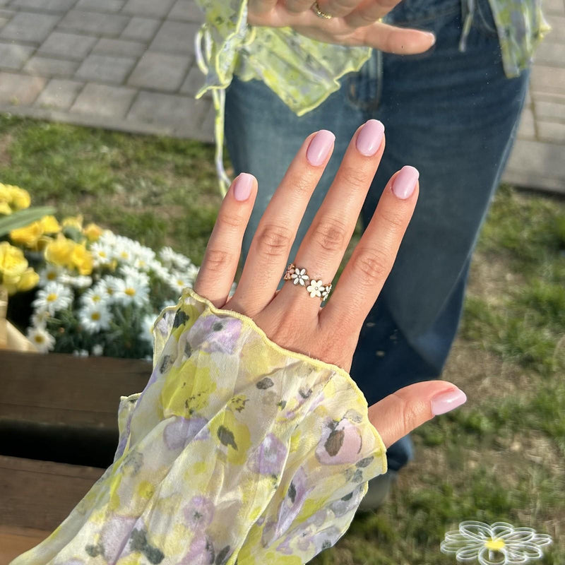 Hand mit rosa Dipping Powder Nägeln, goldenen Blumenring, Bluse mit Blumenmuster und Jeans vor einem Spiegel.
