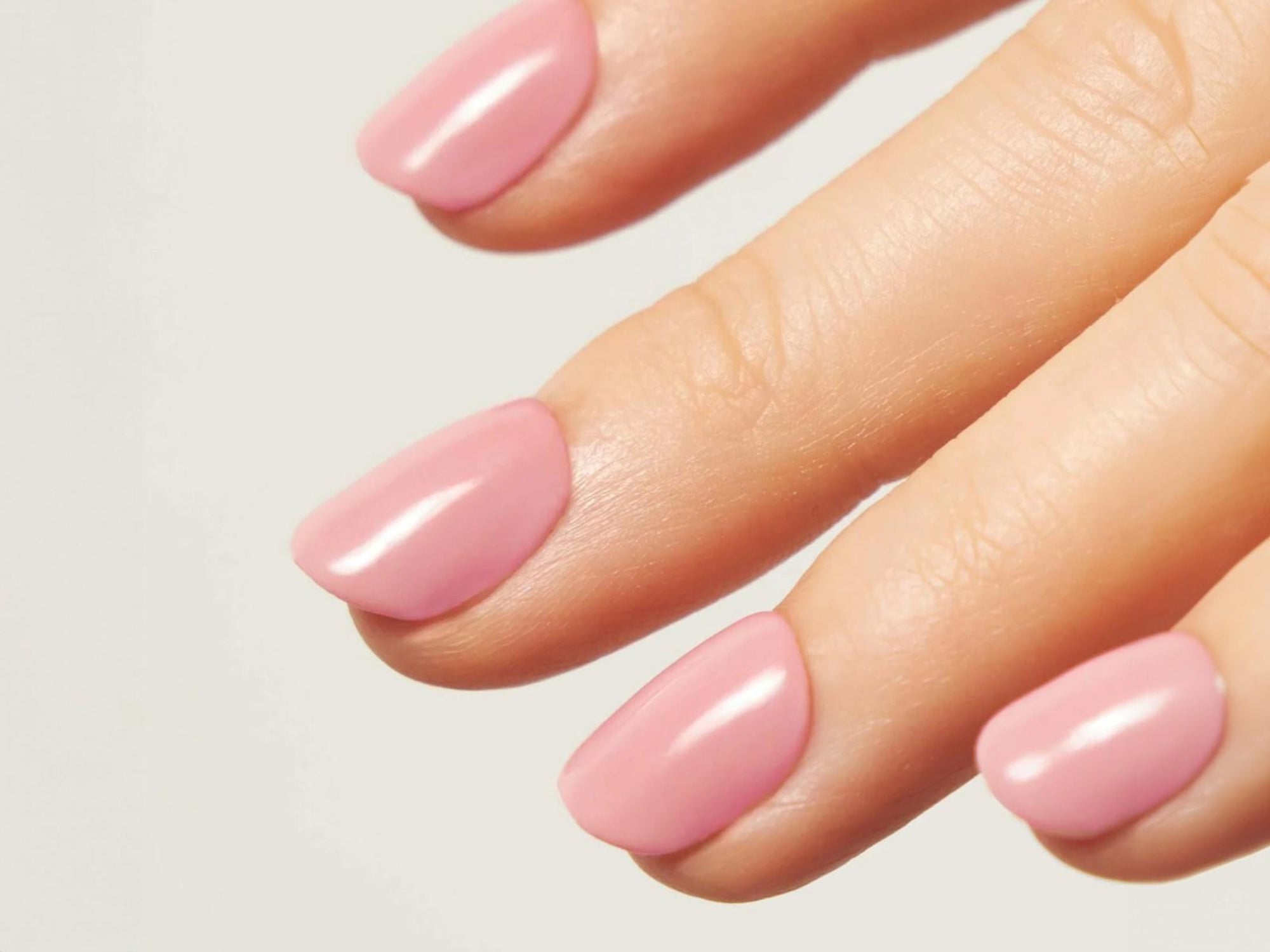 Hand mit rosa Dipping-Powder-Nägeln vor weißem Hintergrund.