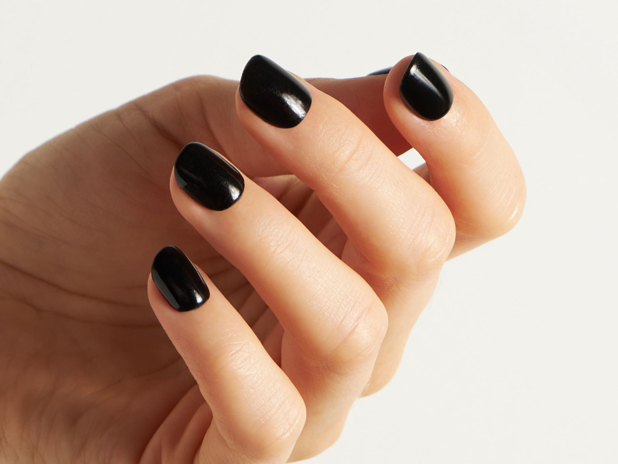 Hand mit schwarzen Dipping Powder Nägeln vor weißem Hintergrund.