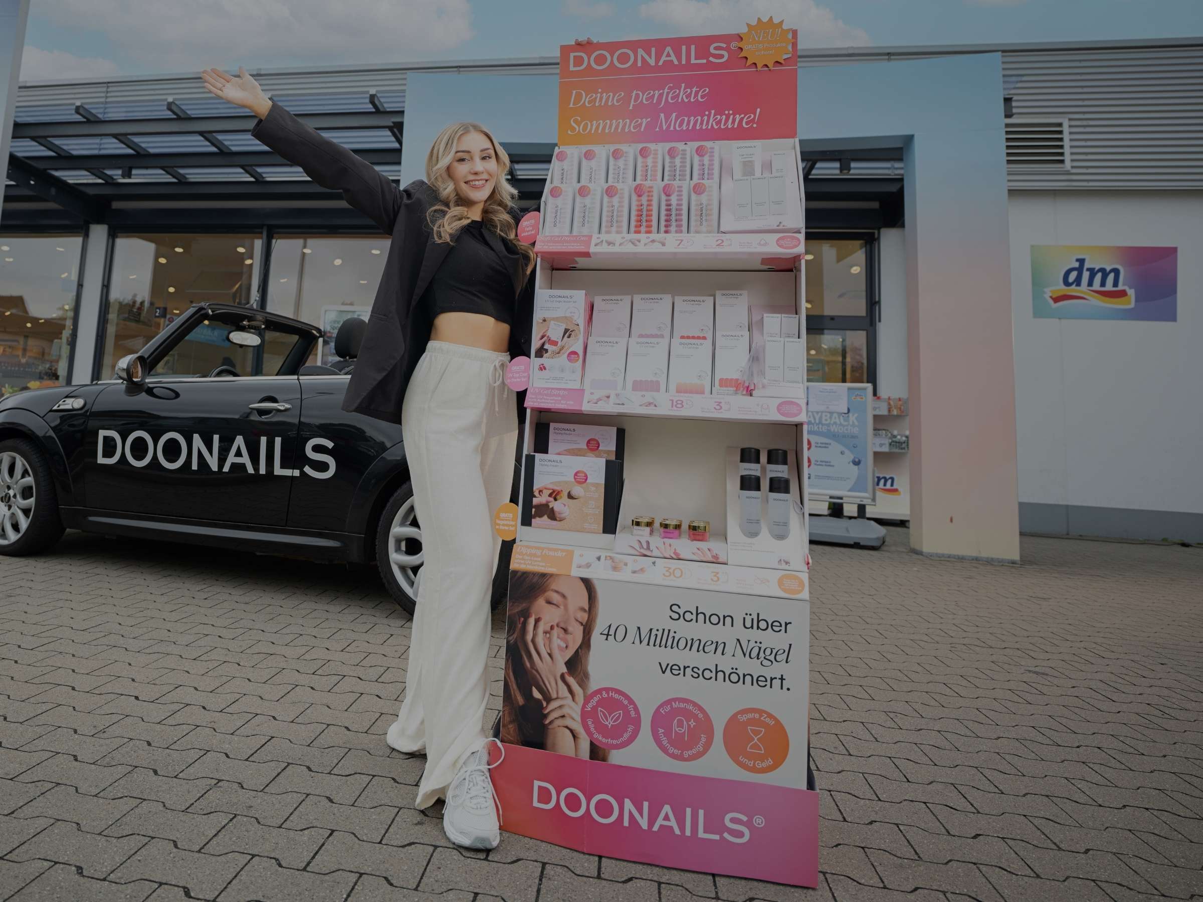Lächelnde Frau mit dem Bodenaufsteller vor dem dm-Markt